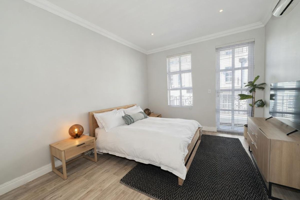 A well-maintained bedroom featuring light wood-look flooring, recessed ceiling lighting, crown molding, and a wall-mounted air conditioning unit.