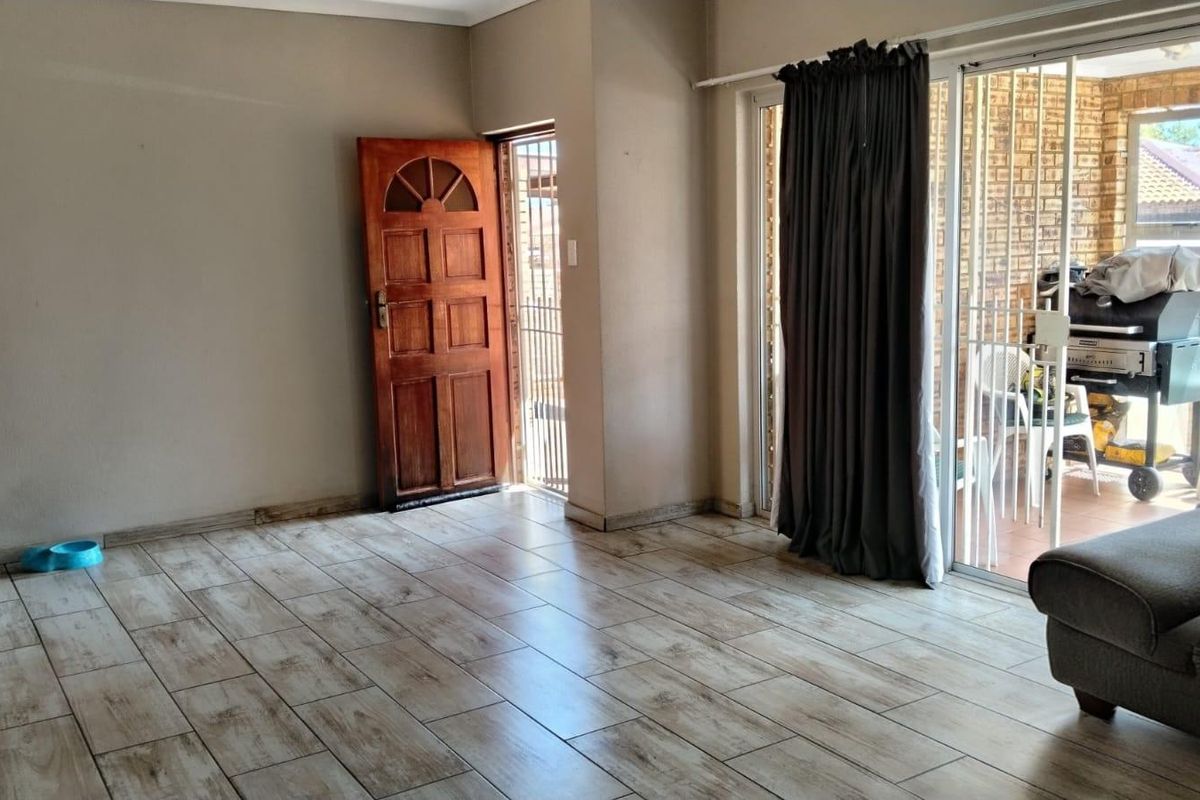 Spacious living area featuring modern wood-look tiled flooring, a solid wooden entrance door, and sliding glass doors leading to an outdoor patio area.