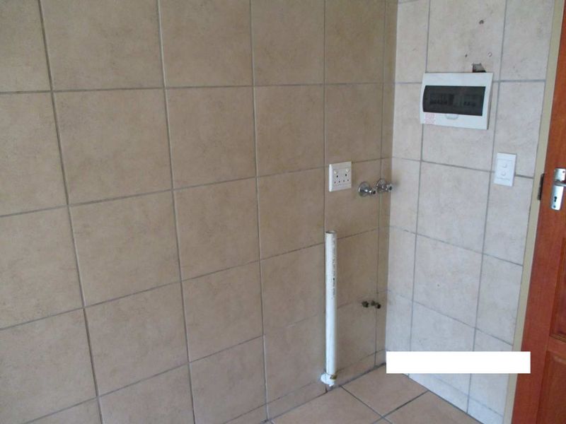 A functional laundry area featuring tiled walls and floor with dedicated plumbing and electrical connections for appliances.