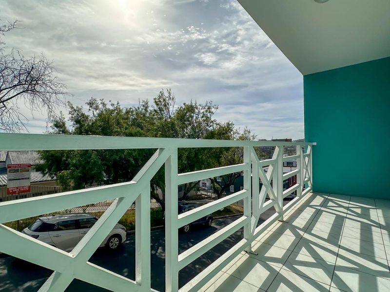 A covered balcony featuring tiled flooring and a white metal balustrade, offering an elevated view of the street and surrounding neighborhood.
