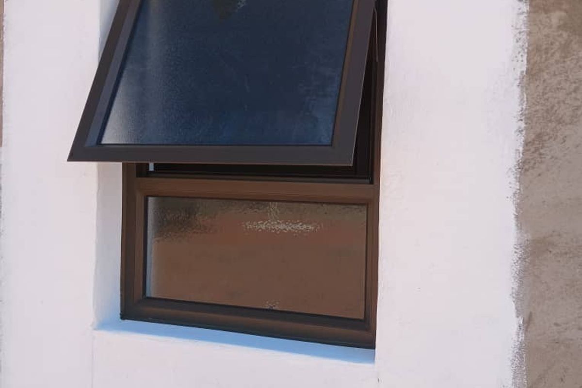 Close-up view of a bronze-framed top-hung window set into an unfinished exterior wall with partial white plastering.