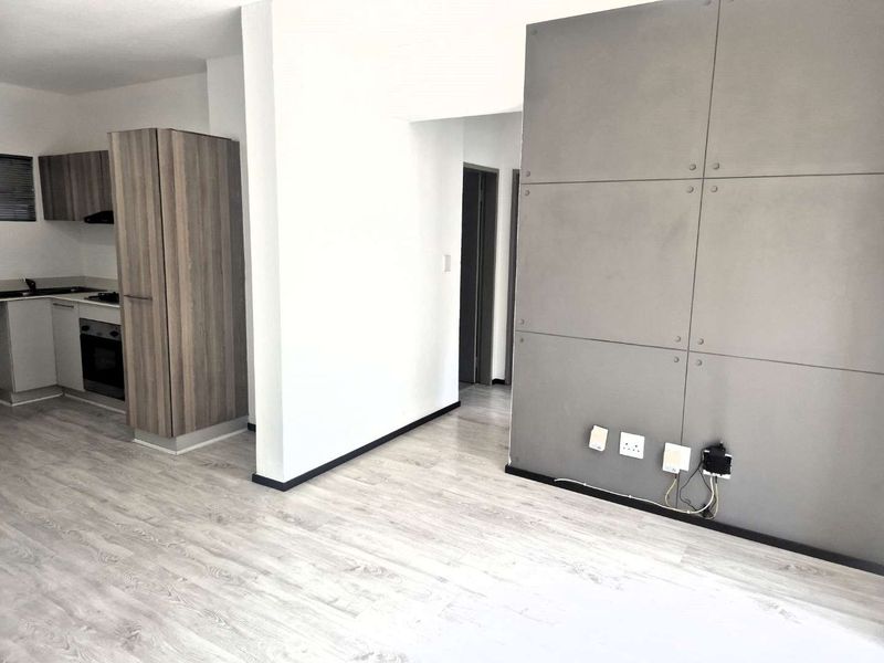 Modern open-plan living area featuring light laminate flooring, a contemporary kitchen with built-in appliances, and a stylish grey feature wall.