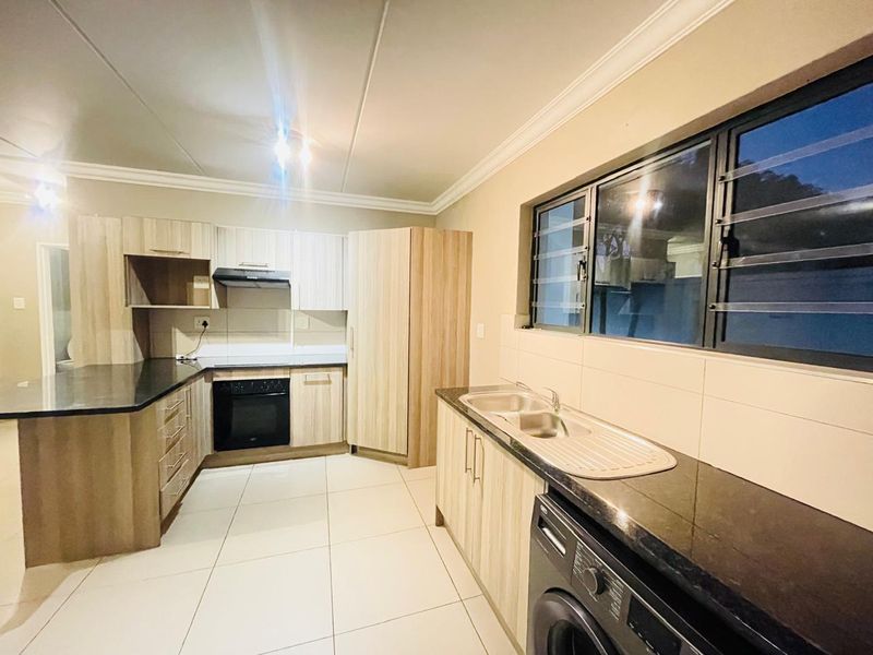 A modern, well-maintained kitchen featuring light wood cabinetry, dark granite countertops, built-in oven, extractor fan, and tiled flooring.