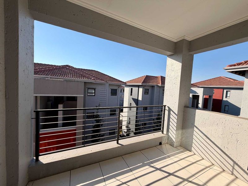 A covered balcony featuring tiled flooring and a metal balustrade, offering an open view of the surrounding apartment complex buildings.