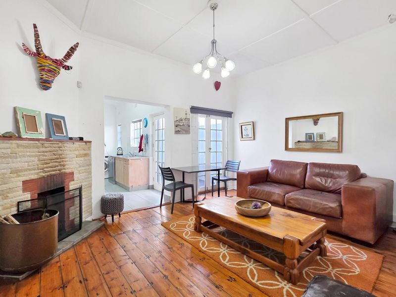 Open plan living area featuring timber flooring, a stone fireplace, and direct access to a functional kitchen space with tiled floors.