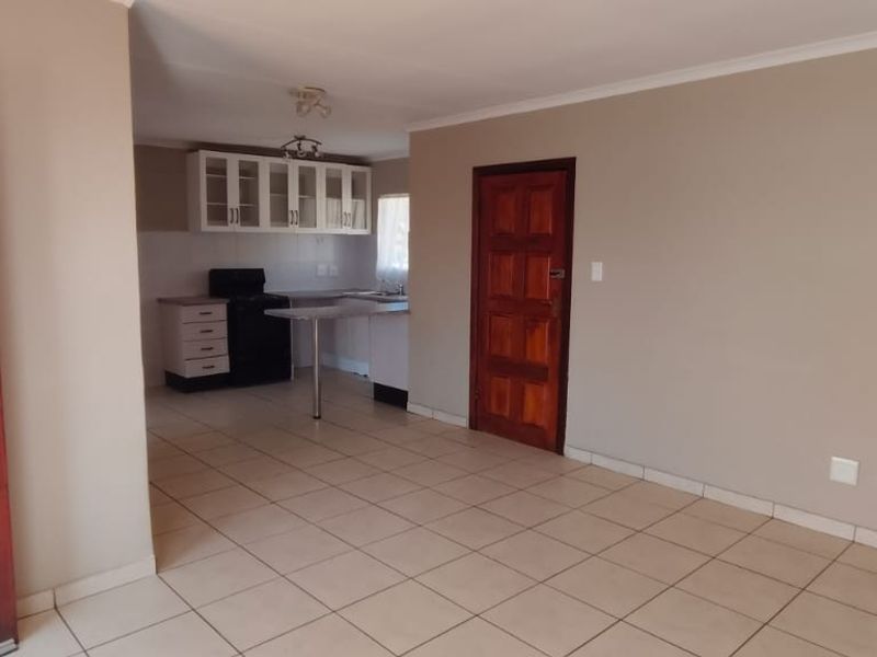 An open-plan living and kitchen area featuring tiled flooring, neutral wall tones, and a functional kitchen layout with built-in cabinetry and a breakfast counter.
