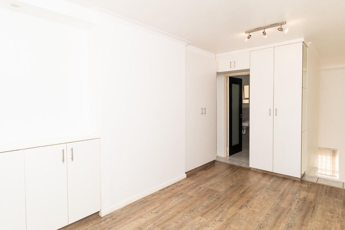 A bright, empty bedroom featuring modern laminate flooring, extensive built-in cupboard storage, and clean white finishes throughout.
