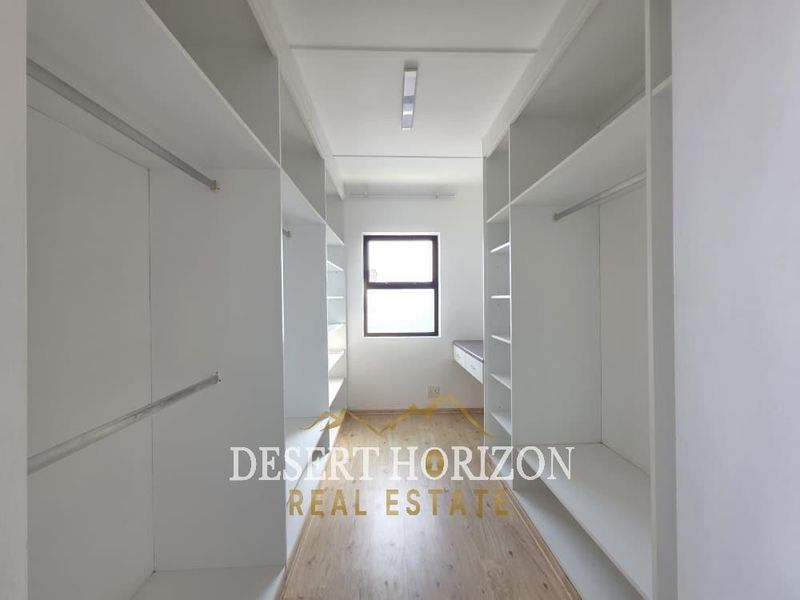 A bright, empty walk-in closet or dressing room featuring extensive built-in white cabinetry, hanging rails, and wood-look laminate flooring.