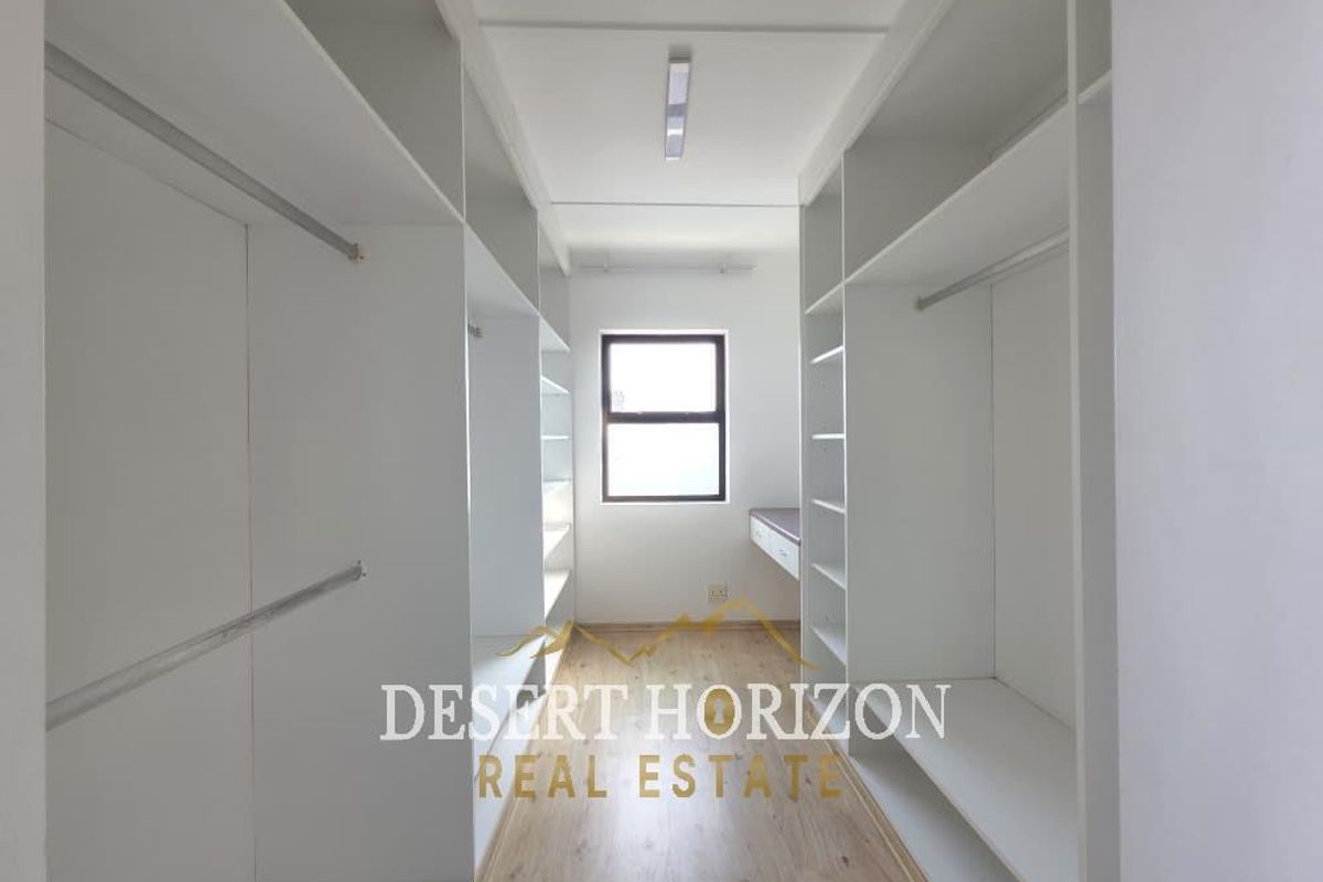 A bright, empty walk-in closet or dressing room featuring extensive built-in white cabinetry, hanging rails, and wood-look laminate flooring.