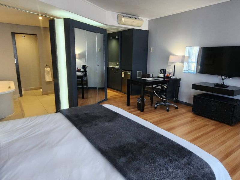 A modern bedroom suite featuring laminate flooring, a built-in mirrored wardrobe, and an open-plan ensuite area with a freestanding bathtub.
