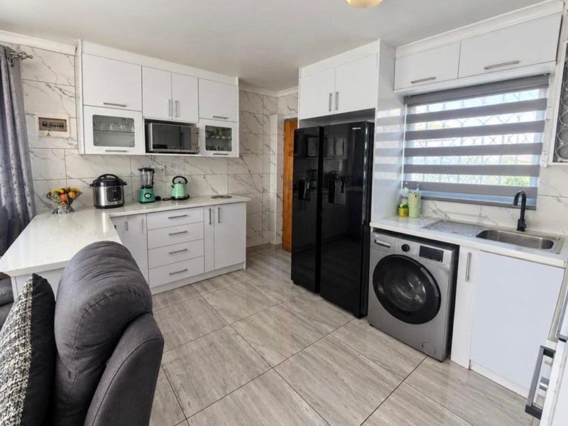Modern kitchen featuring white cabinetry, marble-look wall tiles, integrated sink with black faucet, and tiled flooring.