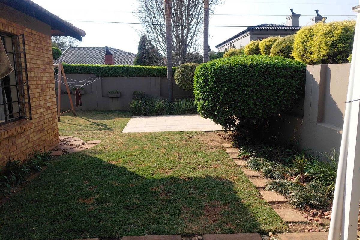 A private rear garden featuring a small paved patio, established hedges, and a lawn area enclosed by brick boundary walls.