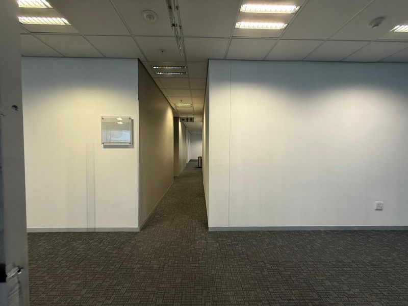 A clean, empty office hallway featuring neutral walls, carpeted flooring, and recessed ceiling lighting, providing access to adjacent office spaces.