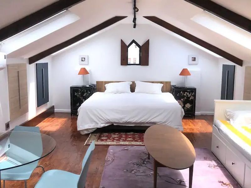 Spacious attic bedroom featuring exposed timber beams, skylight windows, and polished hardwood flooring, creating a bright and airy living space.