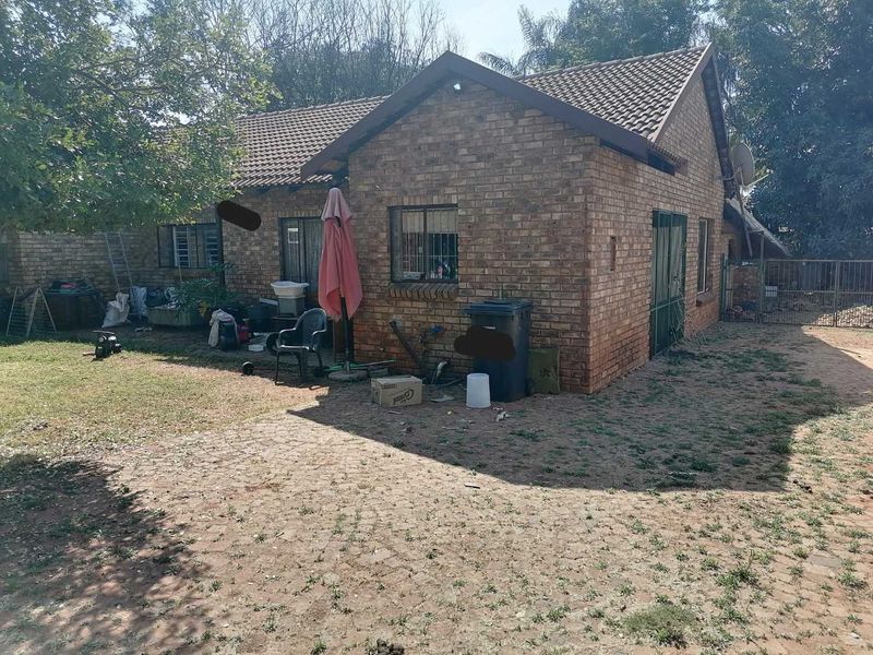Rear view of a face brick house featuring a tiled roof, security bars on windows, and a paved yard area.