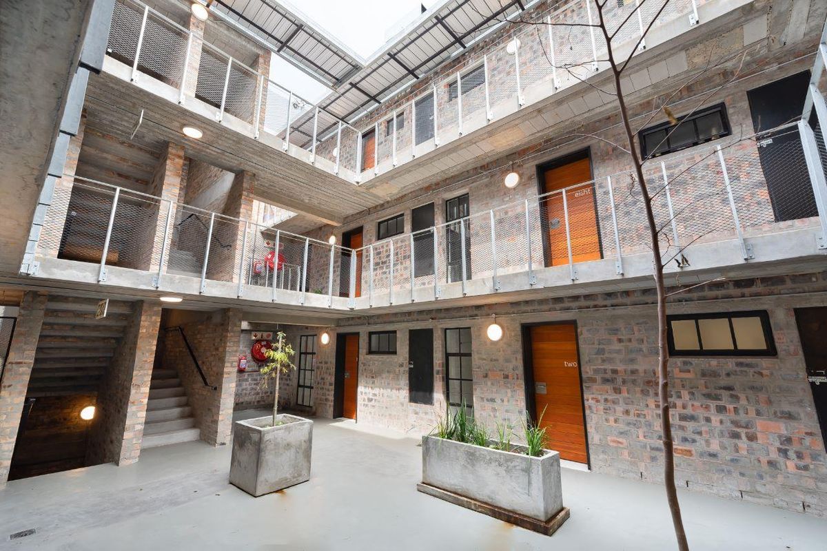 An open-air central courtyard featuring industrial-style exposed brickwork, concrete walkways, and metal mesh balustrades providing access to apartment units.