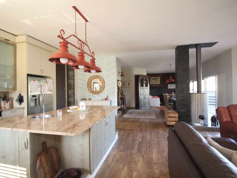 Spacious open-plan living area featuring a modern kitchen with a granite island, hardwood flooring, and a striking stone-clad wood-burning fireplace.