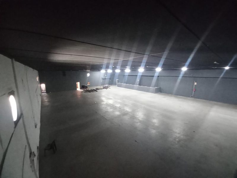 A large, open-plan industrial utility space featuring concrete flooring, dark painted walls, and overhead recessed lighting, suitable for storage or workshop use.