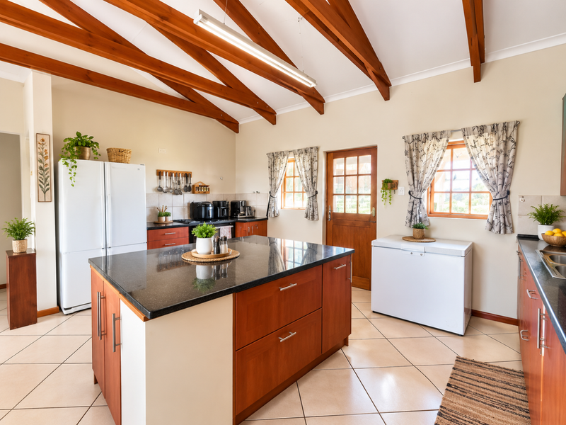 Spacious kitchen featuring a large granite-topped island, exposed timber ceiling beams, and ample wooden cabinetry, creating a warm and functional cooking space.
