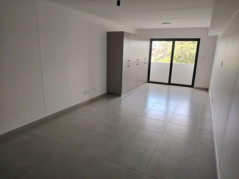 A bright, empty bedroom featuring neutral tiled flooring, built-in cupboards, and a sliding glass door providing access to an outdoor area.