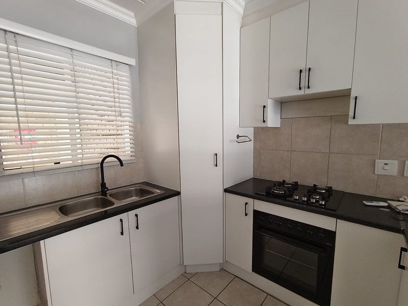 A modern, well-maintained kitchen featuring white cabinetry, dark countertops, a gas hob, built-in oven, and a double sink with a contemporary black tap.