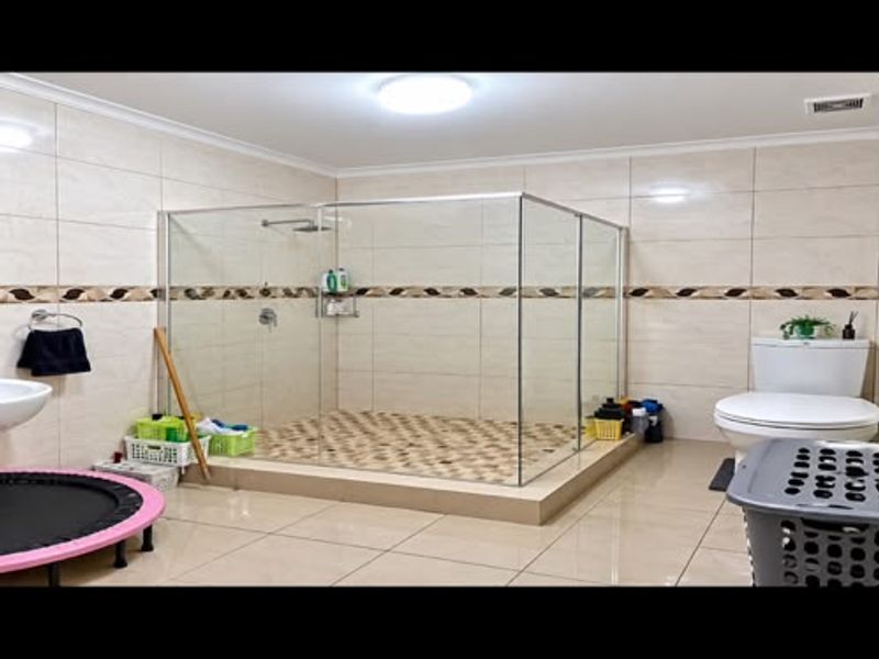 Spacious bathroom featuring a large glass-enclosed walk-in shower with a raised base, neutral ceramic tiling, and a standard toilet.