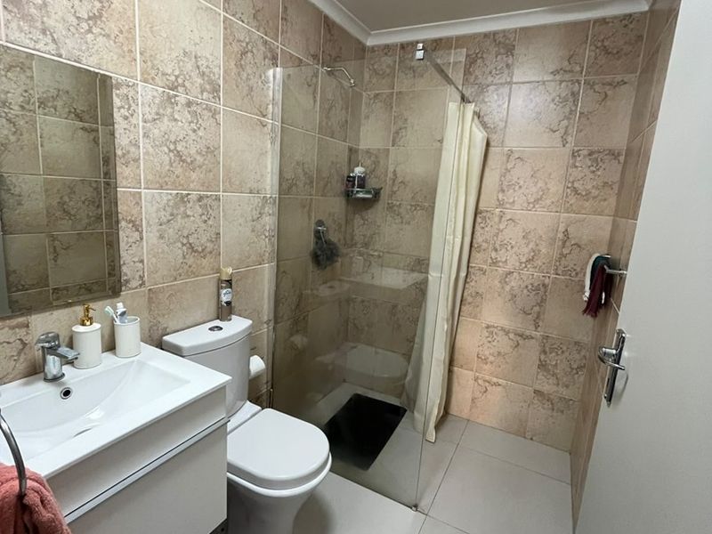 A functional bathroom featuring a modern vanity, toilet, and a glass-enclosed shower with neutral tiled finishes throughout.