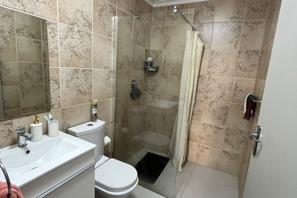 A functional bathroom featuring a modern vanity, toilet, and a glass-enclosed shower with neutral tiled finishes throughout.