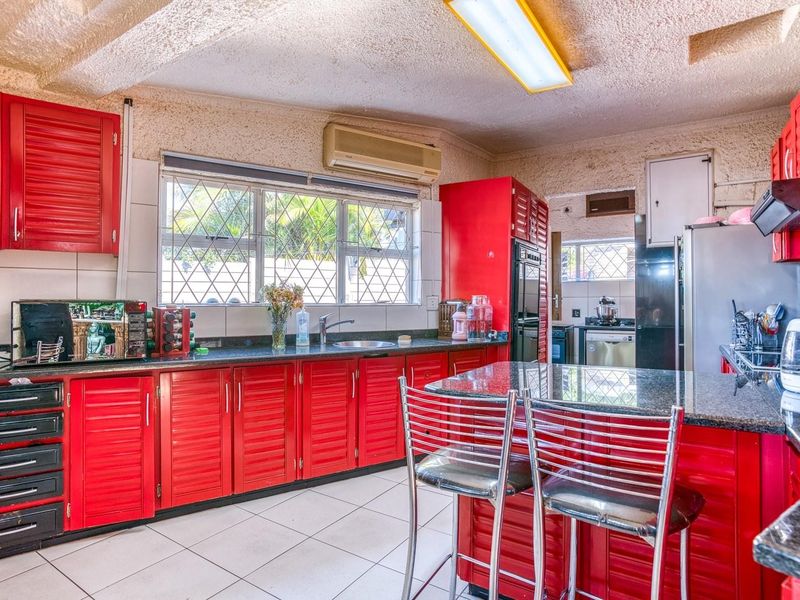 A functional kitchen featuring vibrant red louvered cabinetry, granite countertops, tiled flooring, and a built-in oven, offering a dated but well-maintained workspace.
