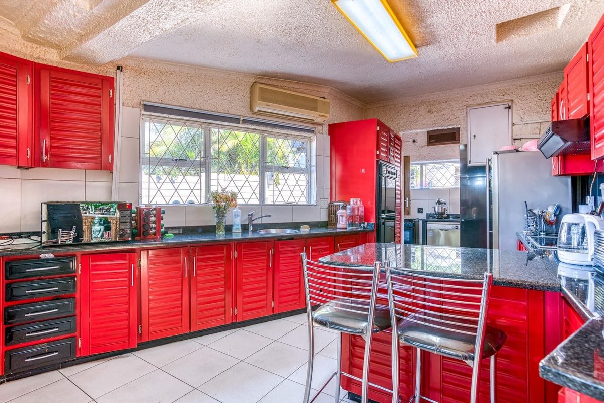 A functional kitchen featuring vibrant red louvered cabinetry, granite countertops, tiled flooring, and a built-in oven, offering a dated but well-maintained workspace.