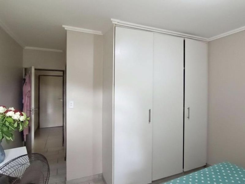 A bedroom featuring neutral wall tones, tiled flooring, and a large white built-in wardrobe with modern handles.