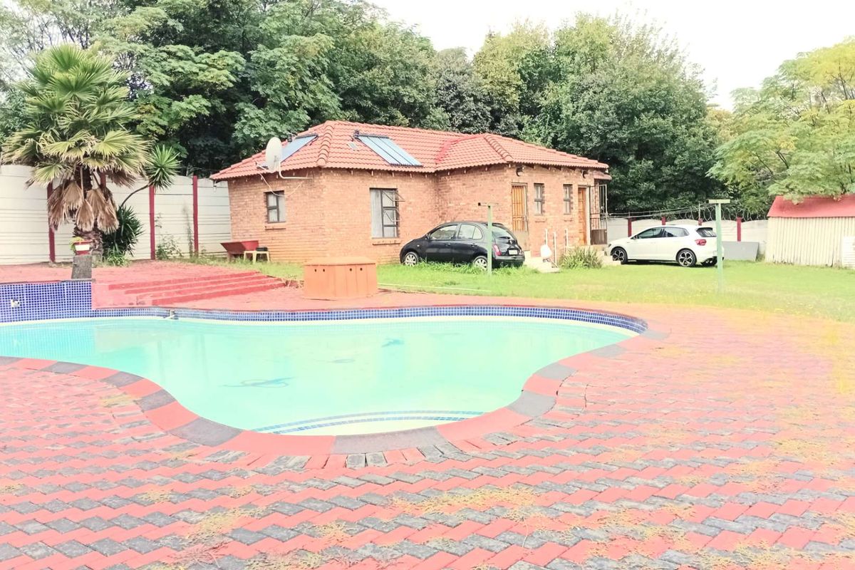 Rear exterior view featuring a swimming pool, brick-paved patio area, and a detached brick house with solar panels.