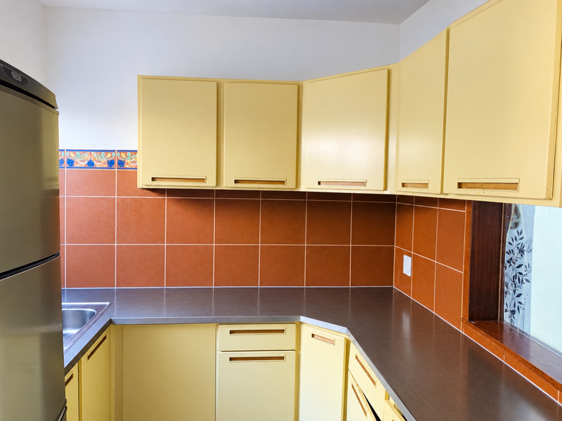 A functional kitchen featuring yellow cabinetry, dark laminate countertops, and terracotta-colored wall tiles with a decorative border.