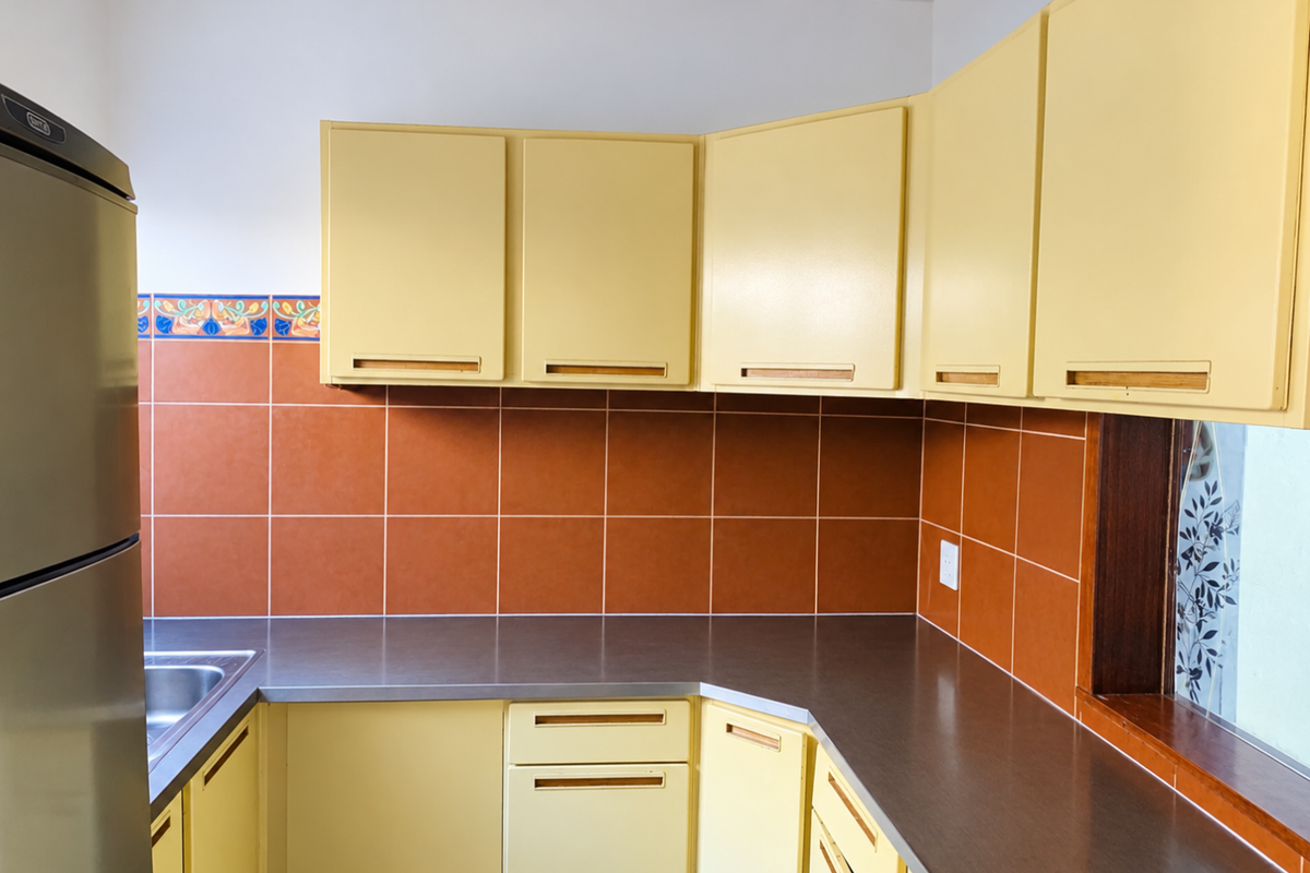 A functional kitchen featuring yellow cabinetry, dark laminate countertops, and terracotta-colored wall tiles with a decorative border.