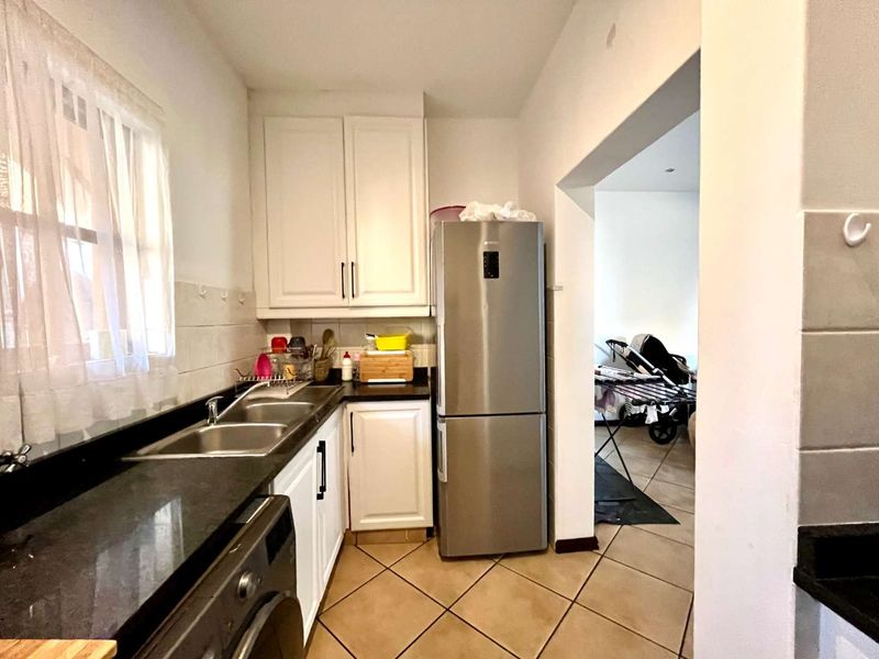 A functional kitchen featuring white cabinetry, dark granite countertops, a double basin sink, and tiled flooring, with an adjacent utility area.
