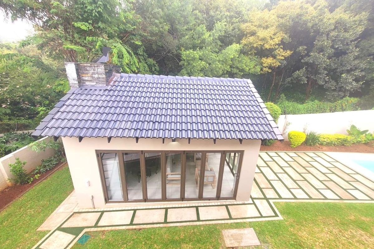 An elevated view of a detached garden structure featuring a tiled roof, stone chimney, and large folding glass doors opening onto a paved patio area.