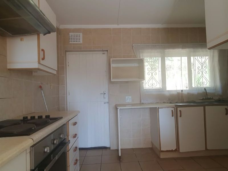 A functional kitchen featuring built-in cabinetry, an electric hob with extractor fan, tiled splashbacks, and a double sink, offering potential for modernization.