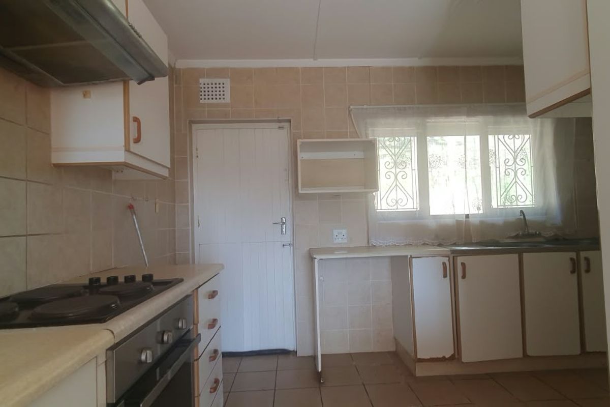 A functional kitchen featuring built-in cabinetry, an electric hob with extractor fan, tiled splashbacks, and a double sink, offering potential for modernization.