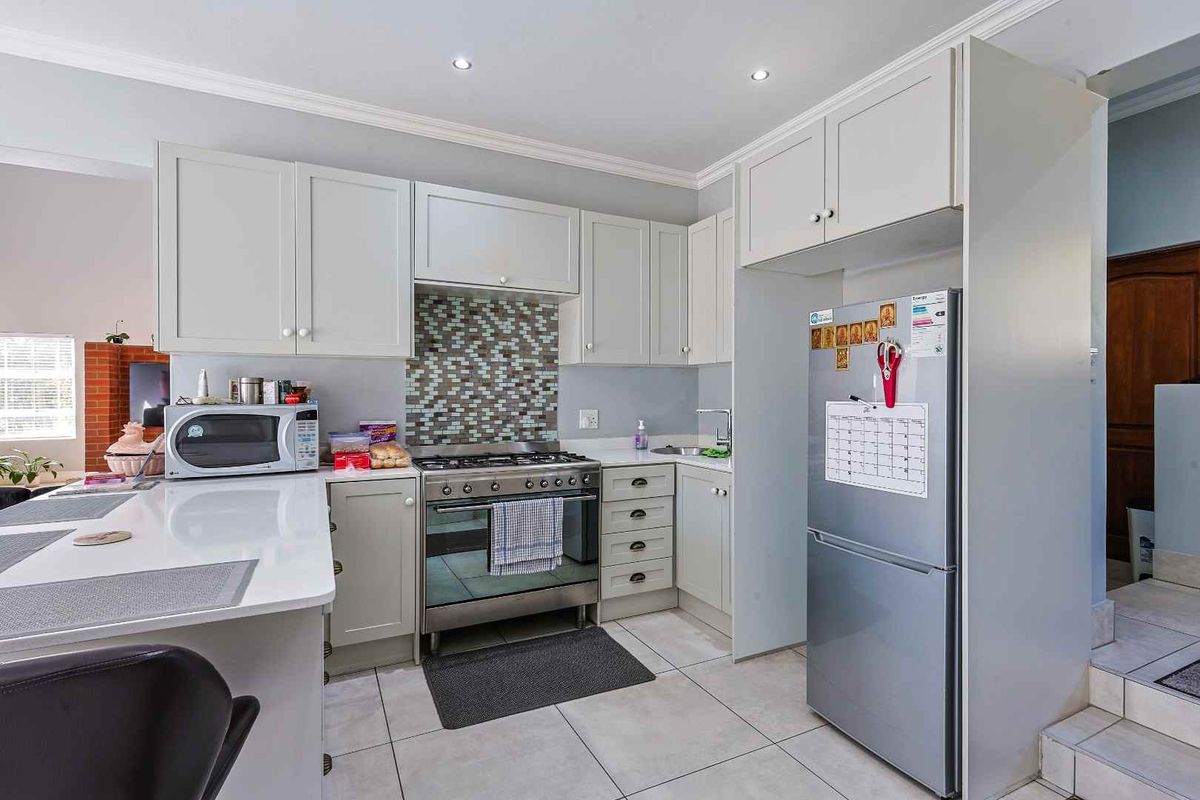 A functional kitchen featuring light-toned cabinetry, a gas stove with a mosaic tile splashback, stone countertops, and tiled flooring.