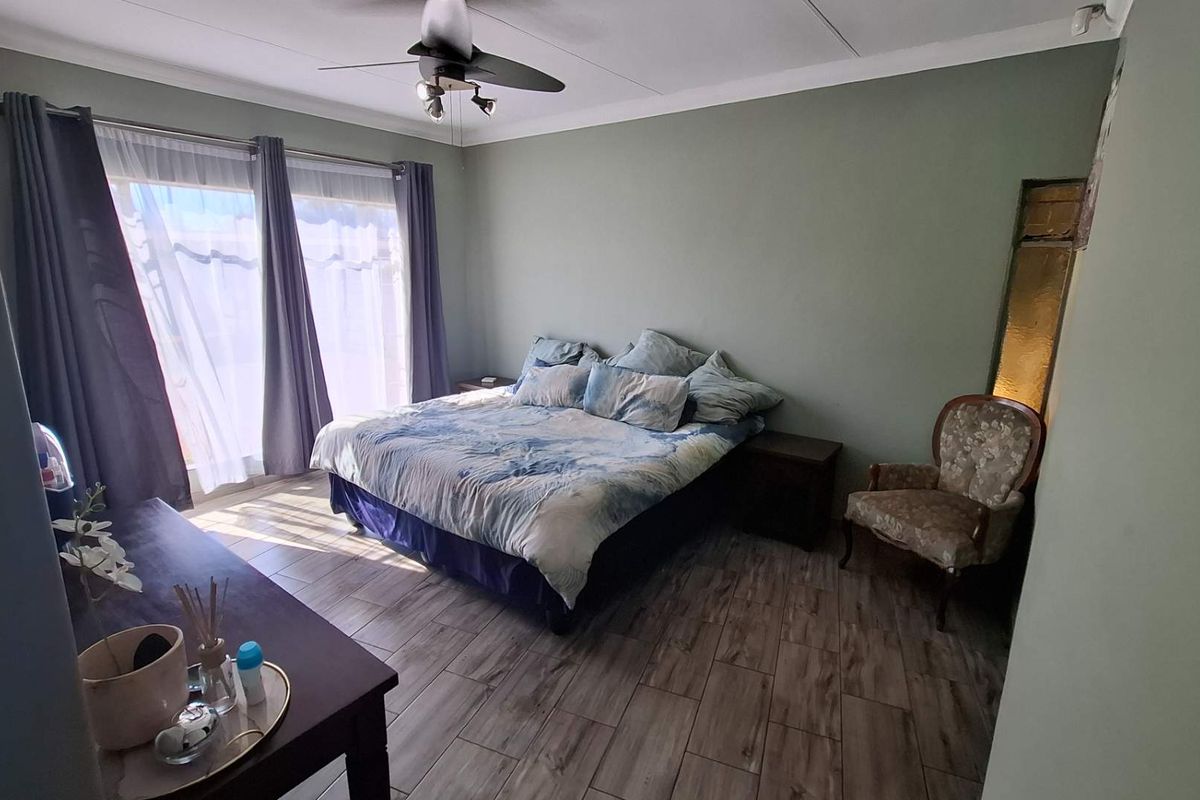 A spacious bedroom featuring wood-look tiled flooring, a ceiling fan, and large sliding glass doors that provide ample natural light.