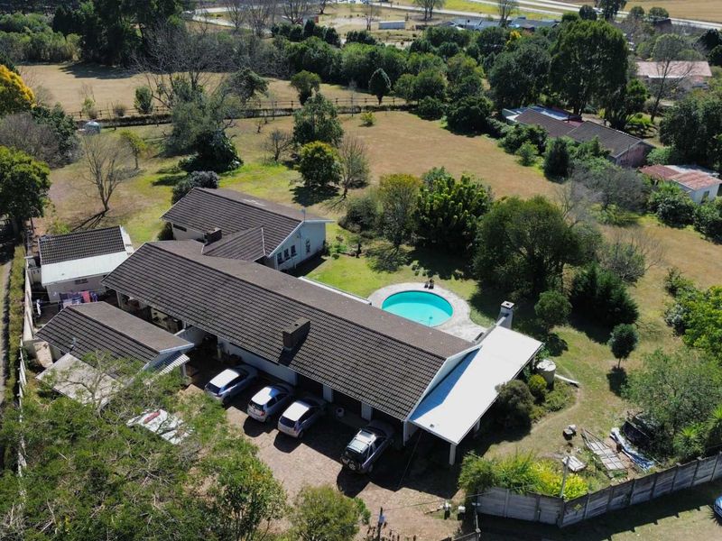 Aerial view of a residential property featuring a large garden, swimming pool, tiled roof house, and paved driveway area.