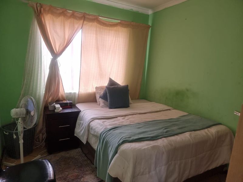 A bedroom featuring a window with curtains and green painted walls showing signs of wear and staining.