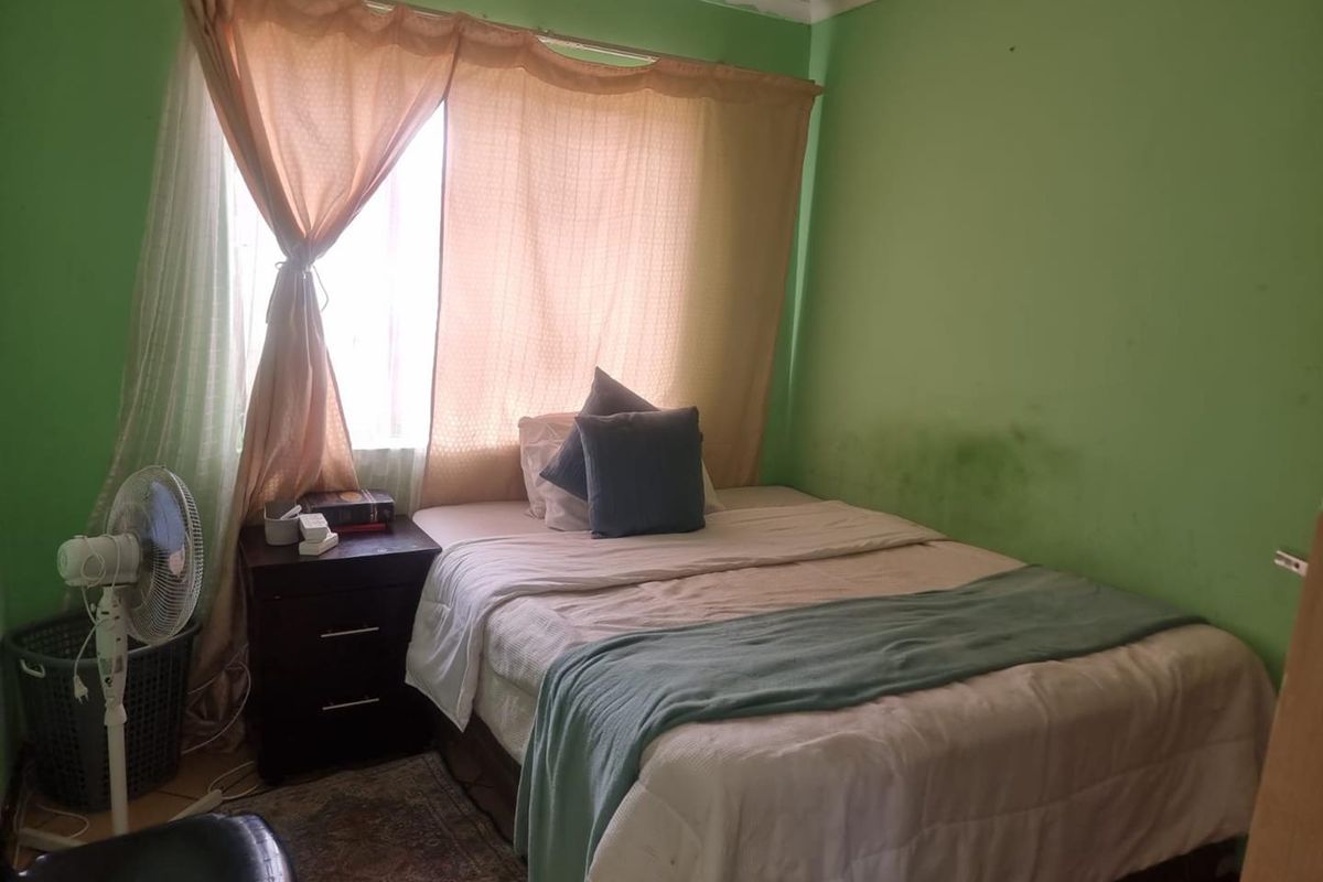A bedroom featuring a window with curtains and green painted walls showing signs of wear and staining.