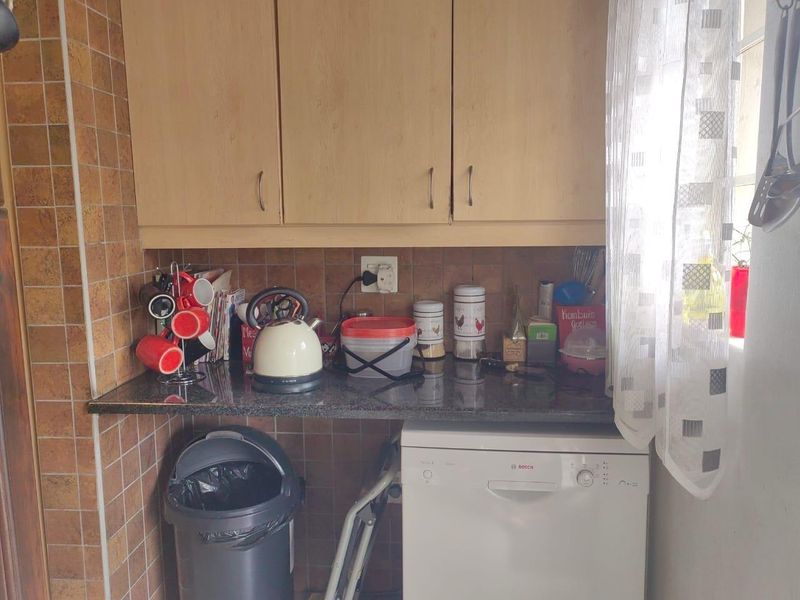 A functional scullery area featuring built-in wooden cabinetry, granite countertops, tiled backsplash, and space for an integrated dishwasher.