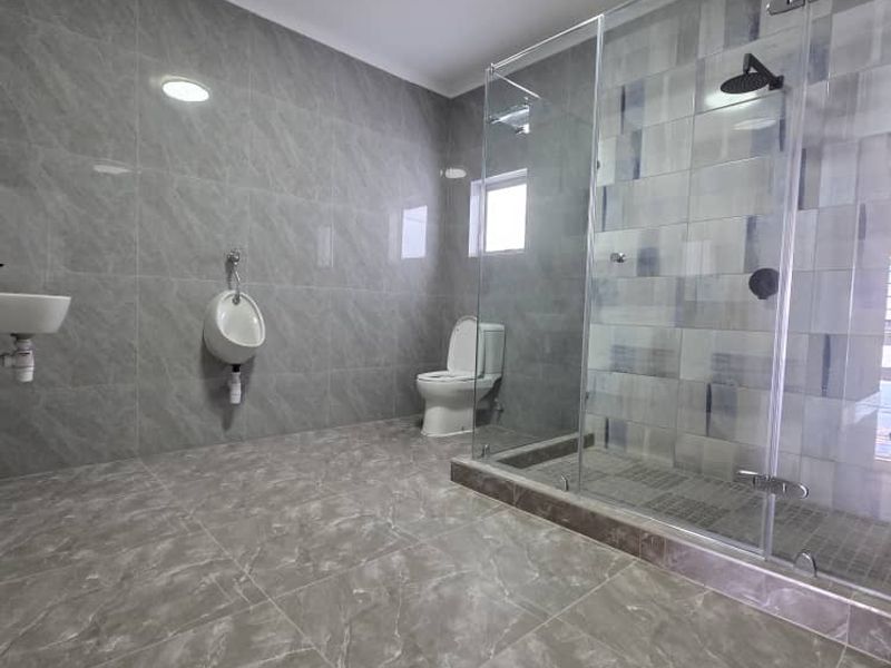 A modern, spacious bathroom featuring grey marble-look tiling, a glass-enclosed shower, a wall-mounted urinal, and a toilet.