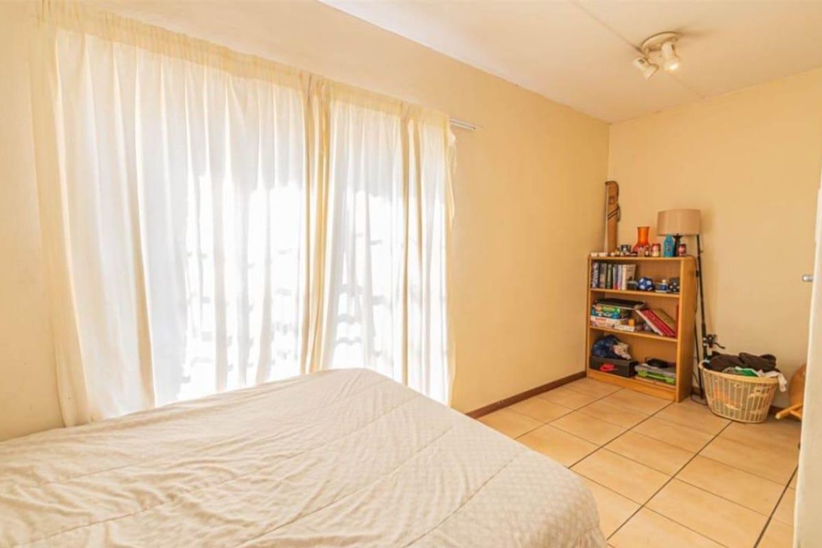 A bedroom featuring tiled flooring and large sliding glass doors with curtains, providing natural light and access to the exterior.
