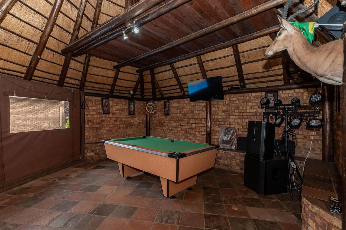 Spacious entertainment area featuring a high-pitched thatch roof, exposed brick walls, and durable tiled flooring, ideal for a games room or social space.