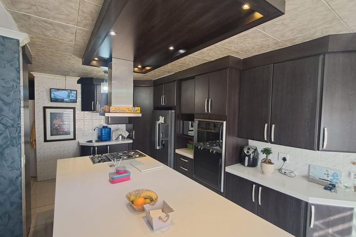 Modern kitchen featuring dark cabinetry, a large central island with a built-in gas hob, and integrated stainless steel oven and extractor fan.