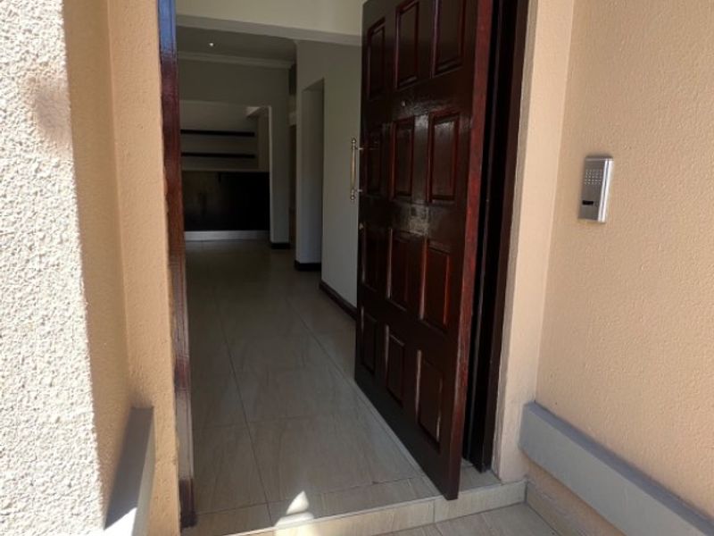 A clean entrance area featuring a solid wood panel door, tiled flooring, and an installed intercom system, leading into an open interior space.