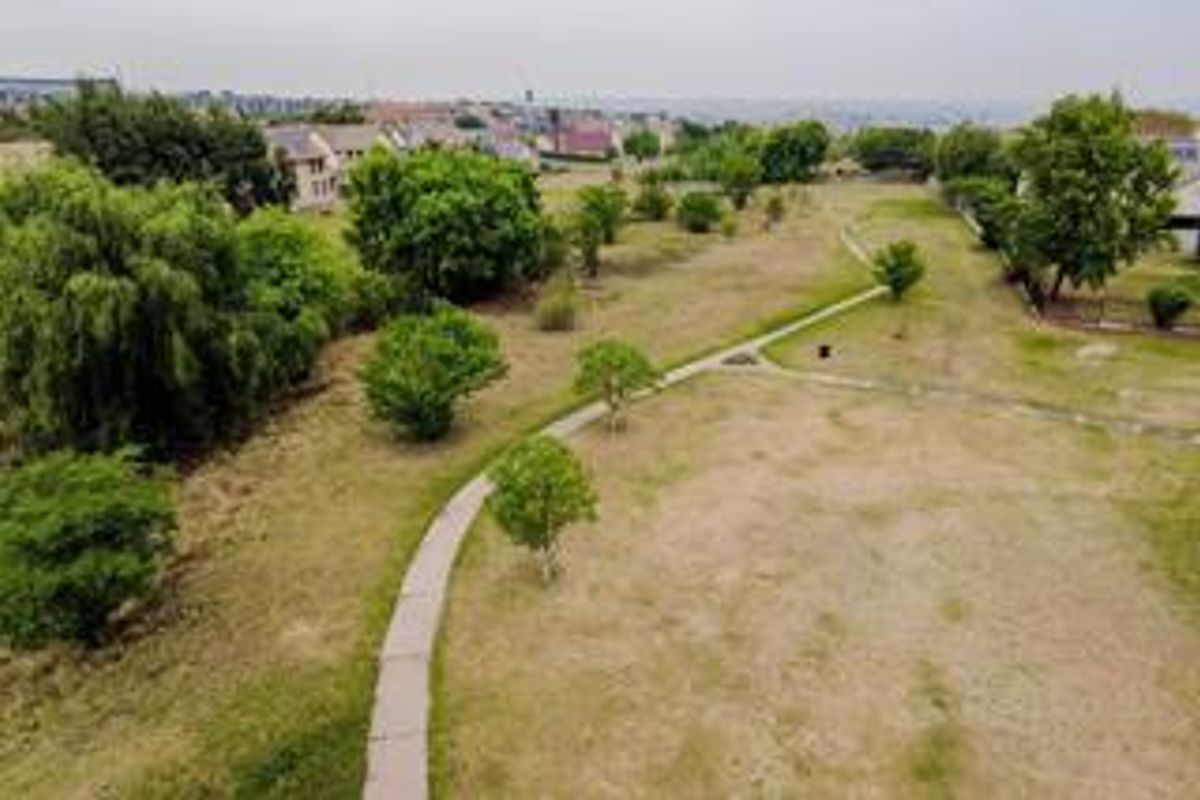 An elevated aerial view of the communal garden area featuring paved pathways and established trees within the residential townhouse estate.